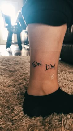 someone with a small tattoo on their ankle saying, swdw in black ink