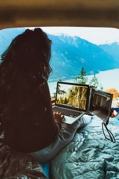 a woman sitting in bed with a laptop computer on her lap looking out the window