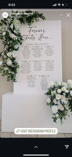 the wedding seating chart is displayed with white flowers and greenery on display next to it