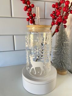 a glass jar that has some red berries in it next to a christmas tree and snowflakes