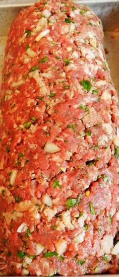 an uncooked meatloaf covered in sauce and herbs