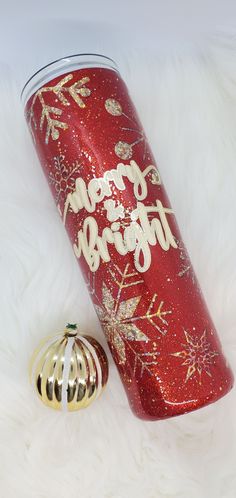 a red and gold christmas tumbler next to an ornament on white fur