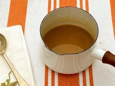 a cup of tea next to a spoon on a striped tablecloth with an orange and white napkin