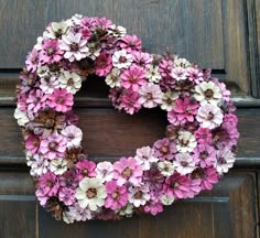 a wreath made out of pink and white flowers on a wooden door with brown trim