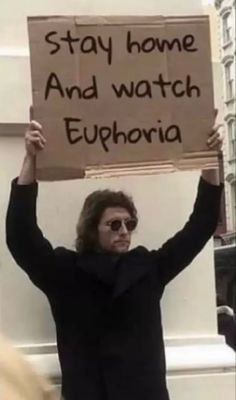 a man holding up a sign that says stay home and watch euphoria