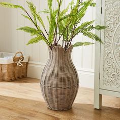 a plant in a wicker vase sitting on the floor next to a white cabinet