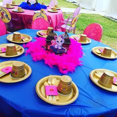 a blue table topped with lots of gold plates and pink napkins covered in feathers