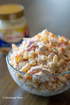 a glass bowl filled with macaroni salad on top of a wooden table