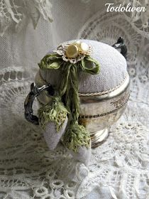 there is a small silver box on the lace tablecloth with flowers and leaves attached to it