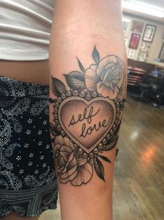 a woman with a tattoo on her arm that reads self love and has flowers in the shape of a heart