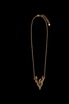 a gold necklace with flowers and leaves hanging from it's sides on a black background