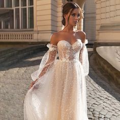 a woman in a white dress standing on a cobblestone street wearing an off the shoulder gown