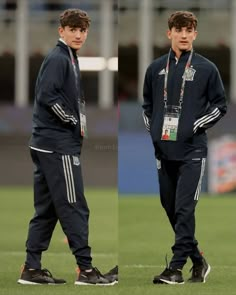 two young men standing next to each other on top of a soccer field with their hands in their pockets