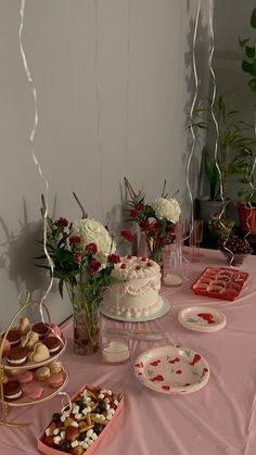 a table topped with lots of desserts next to flowers and plates on top of a pink table cloth