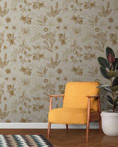 a yellow chair sitting in front of a wall with flowers on it and a potted plant