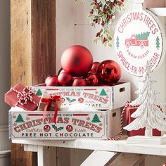 two boxes with christmas trees and ornaments in them sitting on a table next to a potted plant