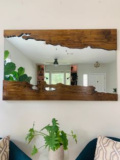 a mirror hanging on the wall above a blue couch with pillows and a potted plant