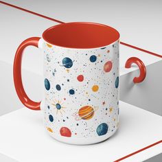 a red and white coffee mug with planets on it sitting on top of a shelf