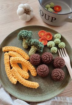 crocheted fruits and vegetables on a plate next to a cup with a fork