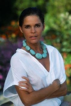 a woman with her arms crossed wearing a white shirt and turquoise necklace on the neck