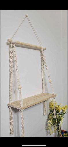 a wooden shelf with rope hanging from it's sides next to a potted plant