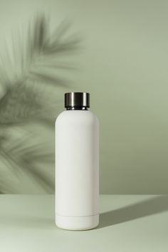 a white bottle sitting on top of a table next to a green wall with a plant in the background