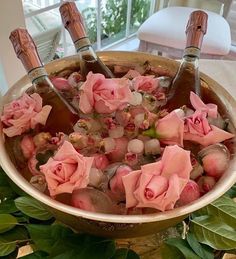 pink roses are in a bowl full of water and rocks with wine corks on the side