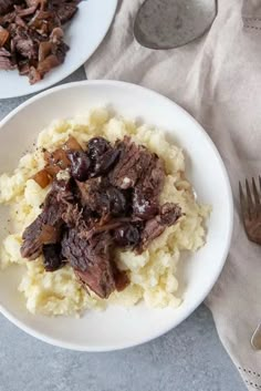 two plates filled with meat and mashed potatoes on top of a table next to utensils