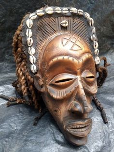 a wooden mask with braids on it's head sitting on top of a rock