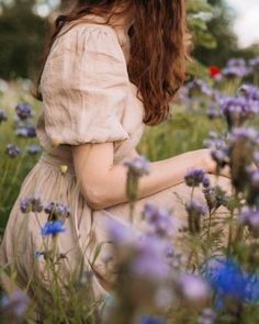 a woman in a field of flowers with her hands on her knees looking at the ground