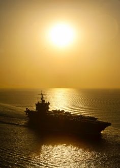 a large ship in the middle of the ocean with the sun setting behind it,