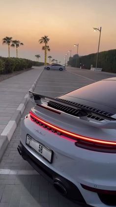 the rear end of a white car parked in front of a parking lot with palm trees