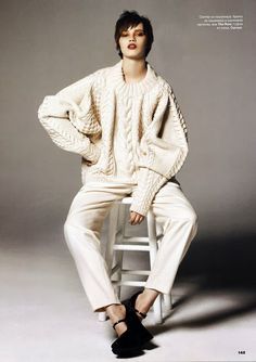 a woman sitting on top of a white chair wearing a sweater and pants with high heels