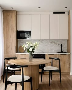 a kitchen with white cabinets and black chairs around a round wooden table in the center