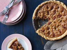 a pecan pie with one slice missing from it on a blue wooden table next to plates and utensils