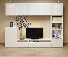 an entertainment center with white cabinets and a black television on the wall, in front of a tree