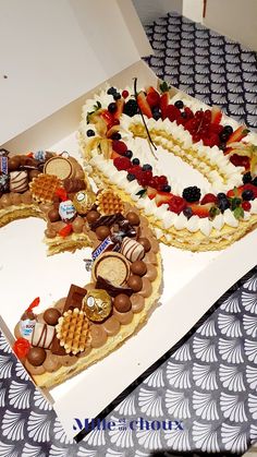 two cakes in the shape of numbers are decorated with fruits and chocolates on display