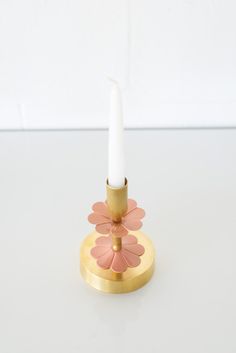 a small candle holder with a single white candle on it's top and pink flowers on the bottom