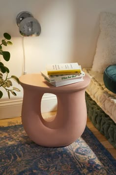 a pink stool sitting on top of a blue rug next to a plant in a living room