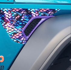 the front end of a blue car with colorful fish scales on it's side