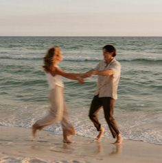 a man and woman dancing on the beach with waves crashing in front of them at sunset