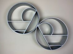 two circular metal shelves on the wall in front of a white wall with an abstract design