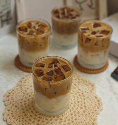 three glasses filled with ice cream on top of a doily next to a book