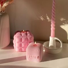 two pink candles sitting on top of a table next to a vase and candle holder