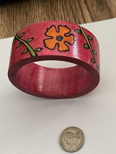 a coin is sitting next to a red wooden bracelet with flowers on it and a flower painted on the side