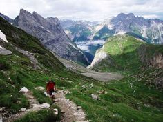 a man hiking up the side of a mountain with green grass and rocks on both sides