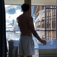 a shirtless man standing in front of a window looking out at the snow covered mountains