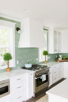 a kitchen with white cabinets and green tile backsplash, an oven and window