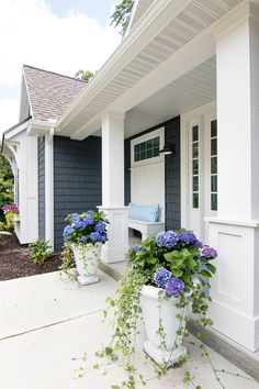 two large white flower pots sitting on the side of a blue and white house with flowers in them