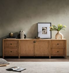 a wooden cabinet with two vases on top of it next to a book shelf